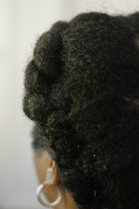 Backview of kinky afro hair loosely plaited into a cornrow.