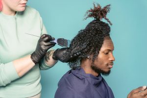 A black man's hair being dyed by a person wearing black gloves.