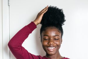 Closeup of a black girl smiling while touching her ponytail hairstyle. 